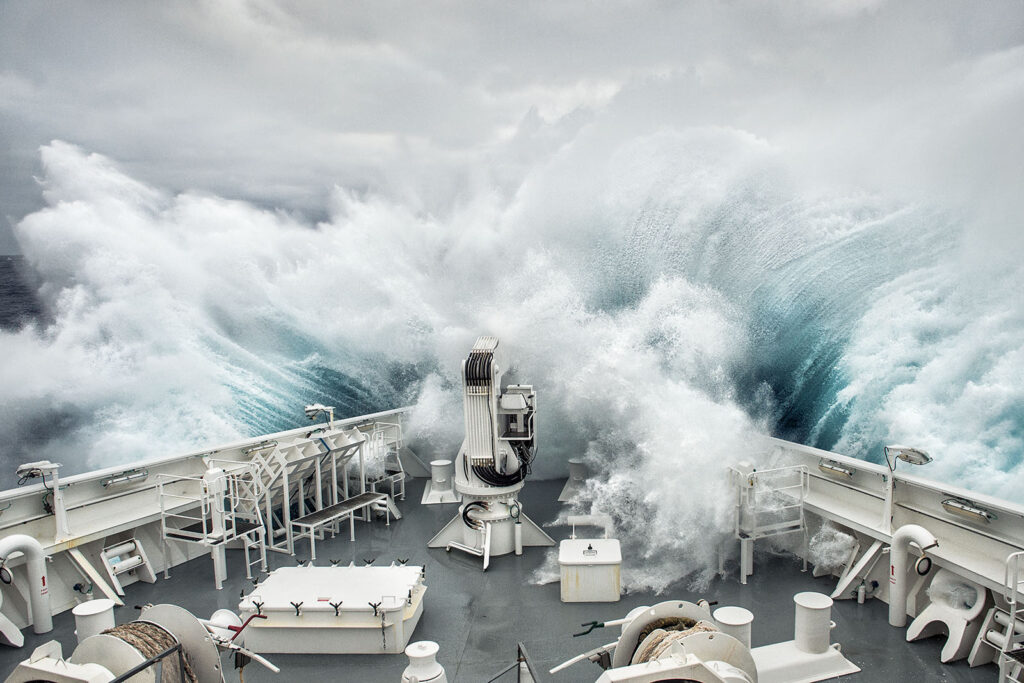 Photographie emblématique. Une vague de 12 mètres de haut frappe de face la proue d'un navire. Vue depuis la passerelle du bateau.